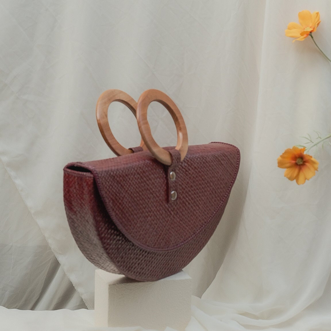 Maroon handbag with wooden handles on a white surface with a light background
