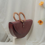 Maroon handbag with wooden handles on a white surface with a light background