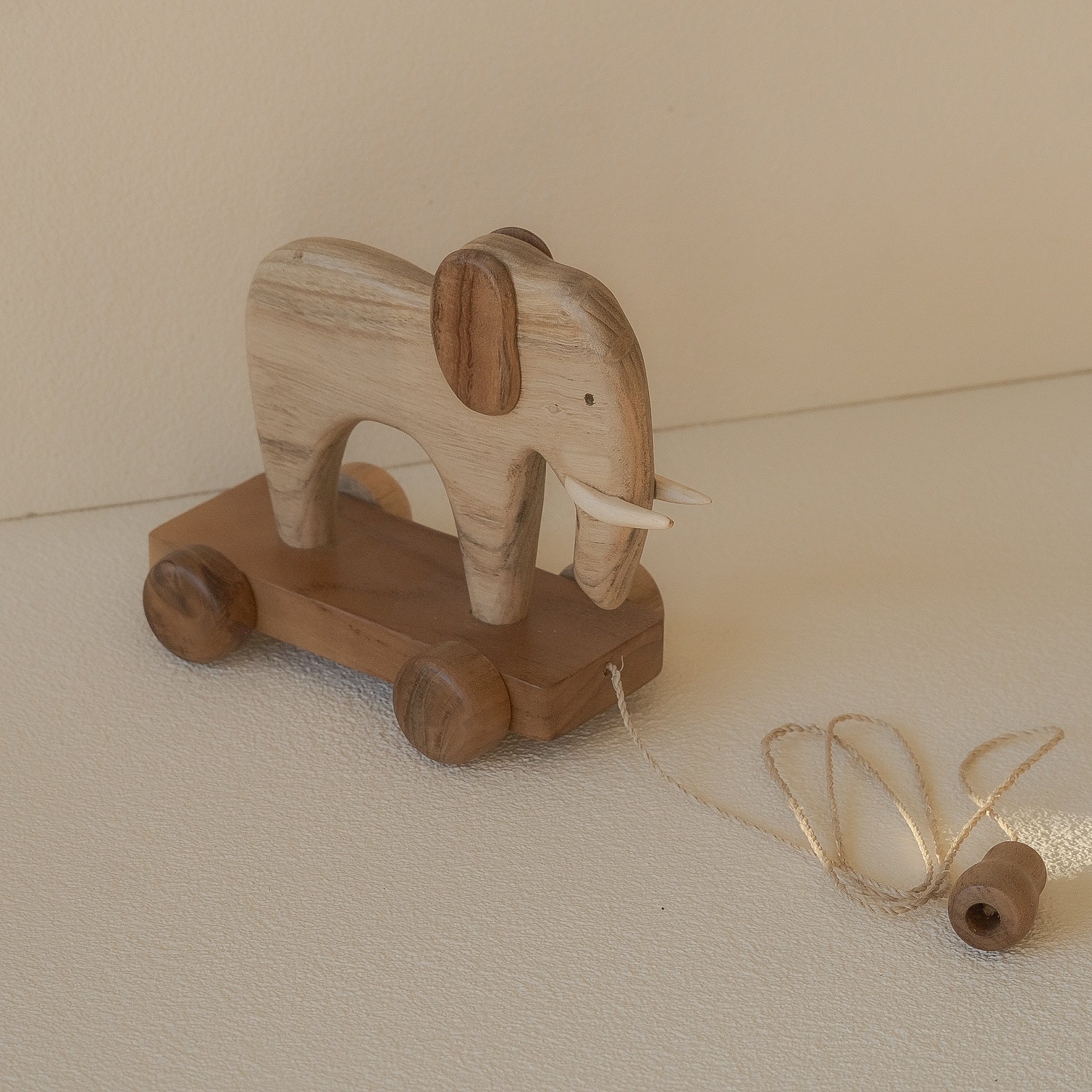Wooden elephant toy with wheels on a beige surface
