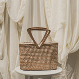 Woven basket with a handle on a white pedestal against a soft, neutral background