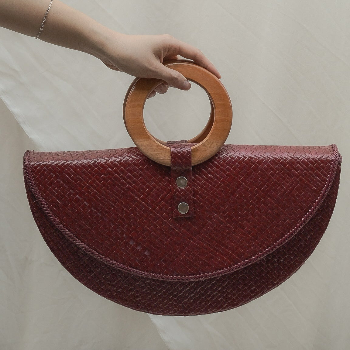 Red handbag with wooden handle held by a person against a neutral background