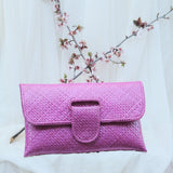 Pink textured clutch bag on a white background with a branch of flowers.