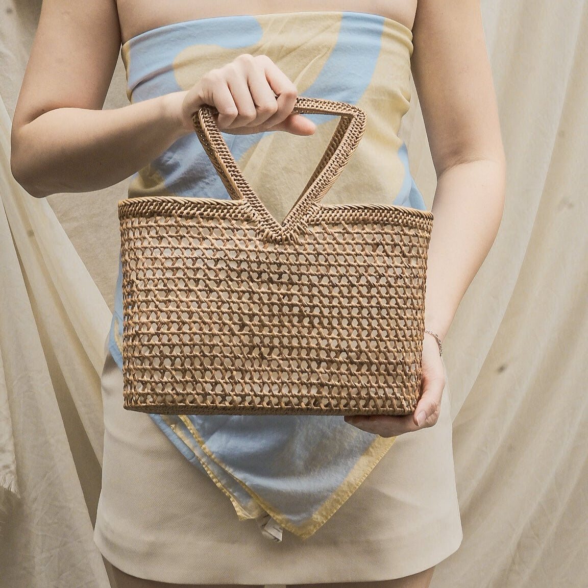 Person holding a woven handbag with a neutral background