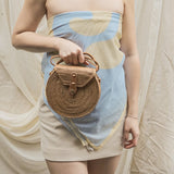 Woman holding a woven handbag wearing a strapless dress with a blue and beige pattern.