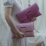 Woman holding two pink clutch bags against a white curtain background