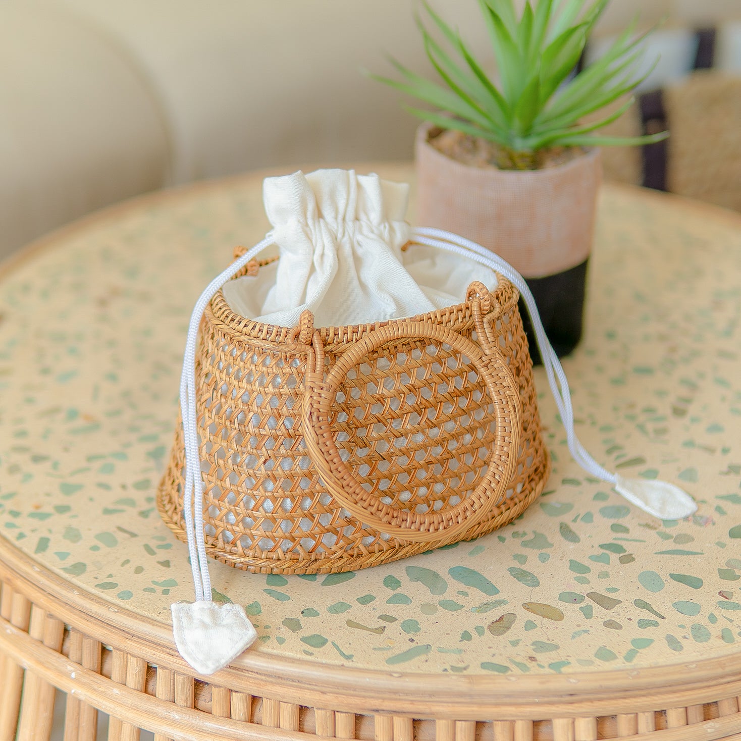 Camilla circle bag with drawstring on a round table with a plant in the background
