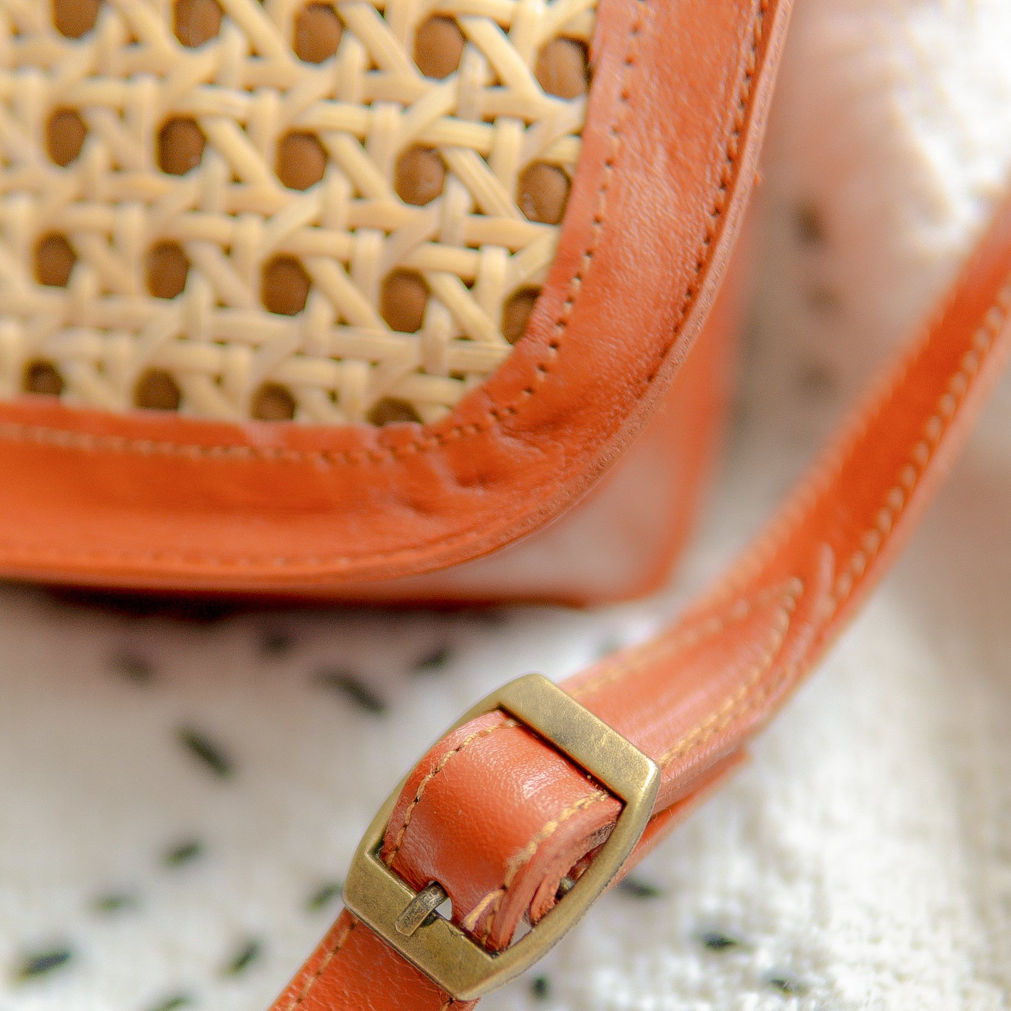 Close-up of an orange handbag with a woven pattern and gold buckle on a textured surface.