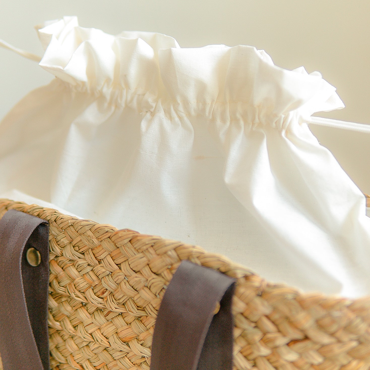 White blouse with ruffled sleeves and a straw bag with a brown cotton strap on a light background