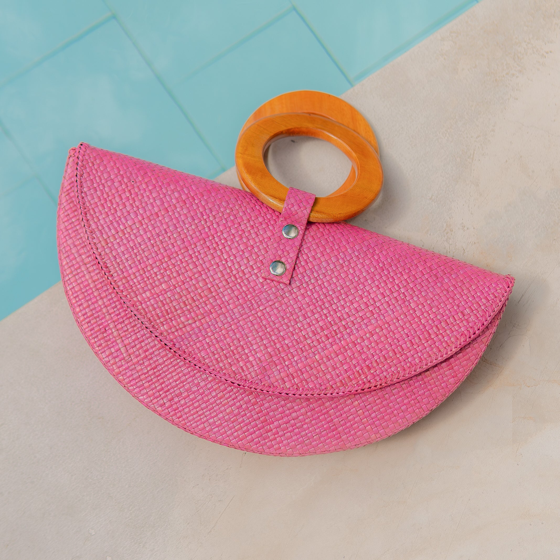 Pink straw bag with orange handle on a light blue and beige background