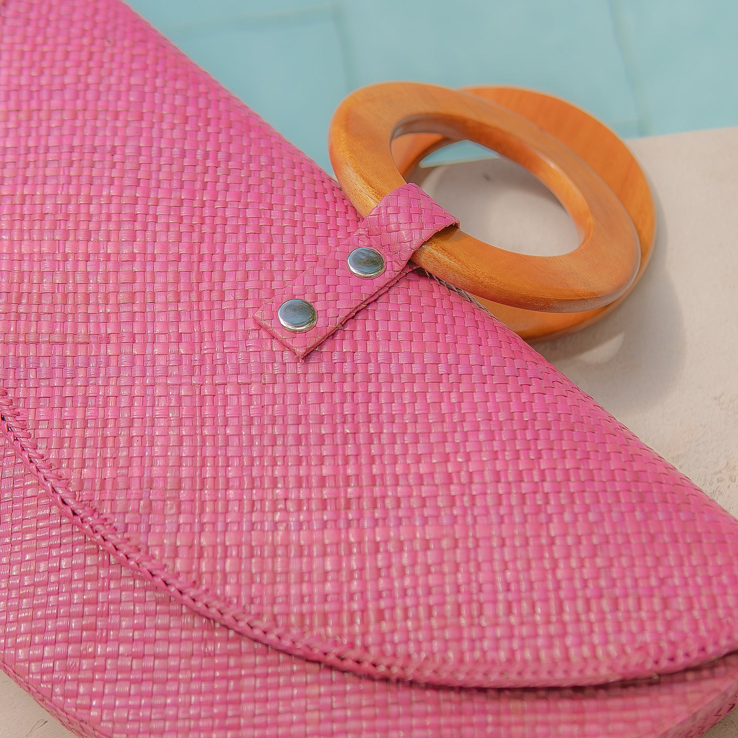 Pink woven bag with orange handles on a light blue background
