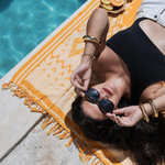 Woman lying on a yellow poolside rug with sunglasses, near a pool.