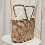 Woven basket with a white drawstring bag on a white stool against a white curtain background