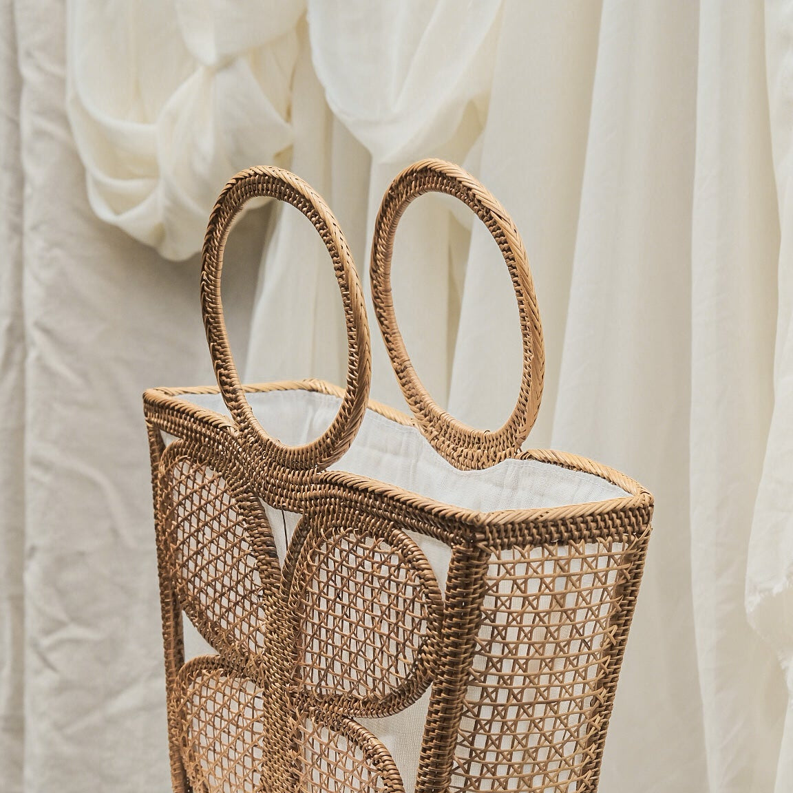 Woven handbag with circular handles on a white stool against a white curtain background