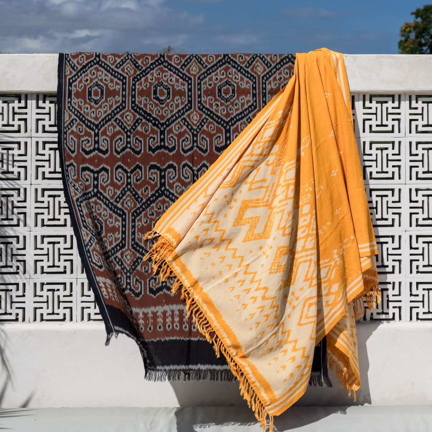 Two patterned towels draped over a white railing with a blue sky background