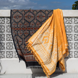 Two patterned towels draped over a white railing with a blue sky background