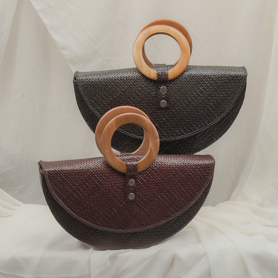 Two handbags with wooden rings on a white fabric background