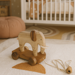 Wooden elephant toy with wheels on a soft surface in a nursery setting