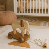Wooden elephant toy with wheels on a soft surface in a nursery setting