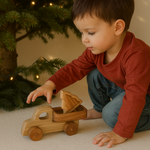 Child playing with a wooden toy truck in front of a decorated Christmas tree.