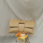 Beige woven clutch bag with a small bouquet of flowers on a white fabric background
