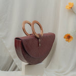 Maroon handbag with wooden handles on a white surface with a light background