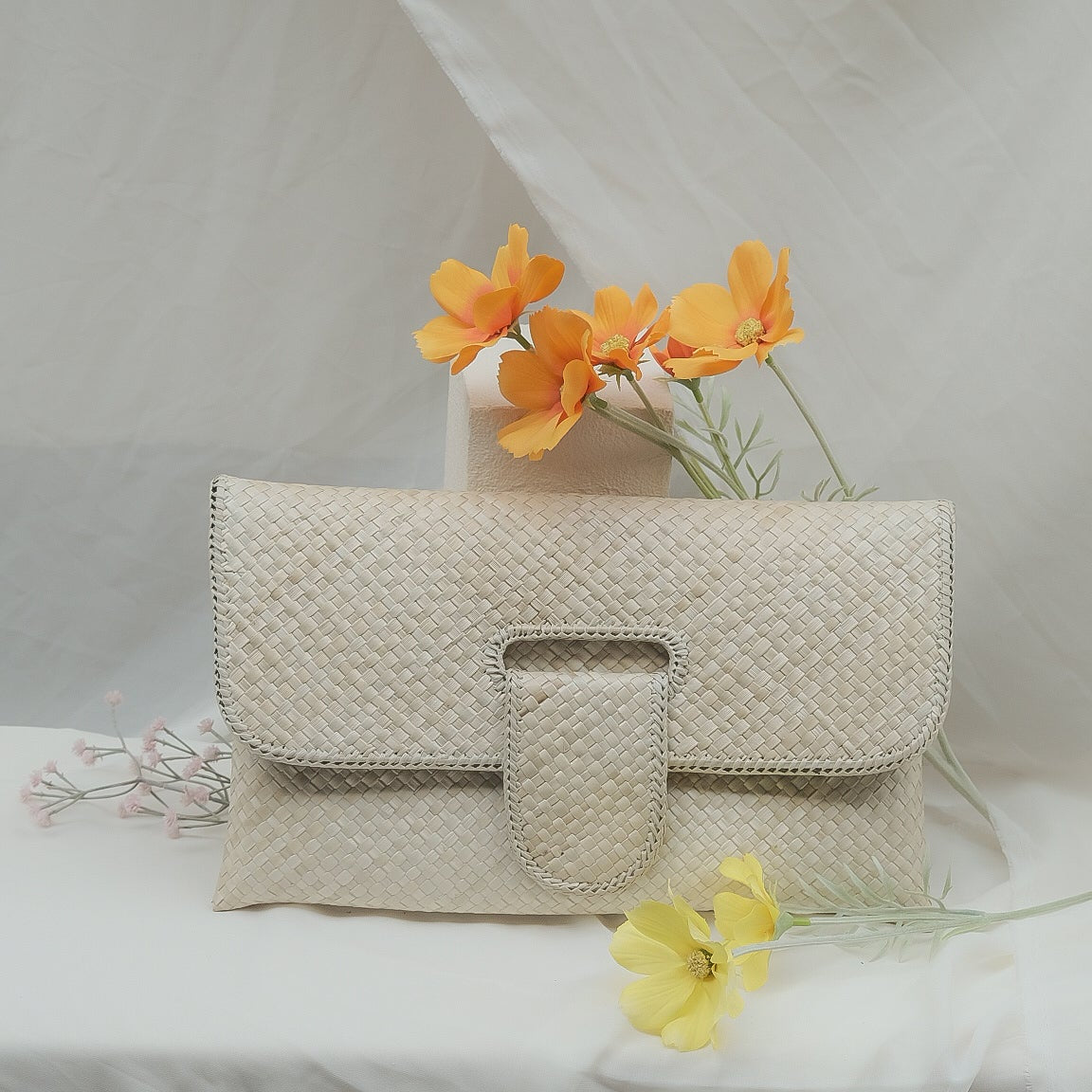 Beige woven handbag on a white fabric background with orange flowers.