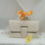 Beige woven handbag on a white fabric background with orange flowers.