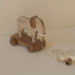 Wooden elephant toy with wheels on a beige surface