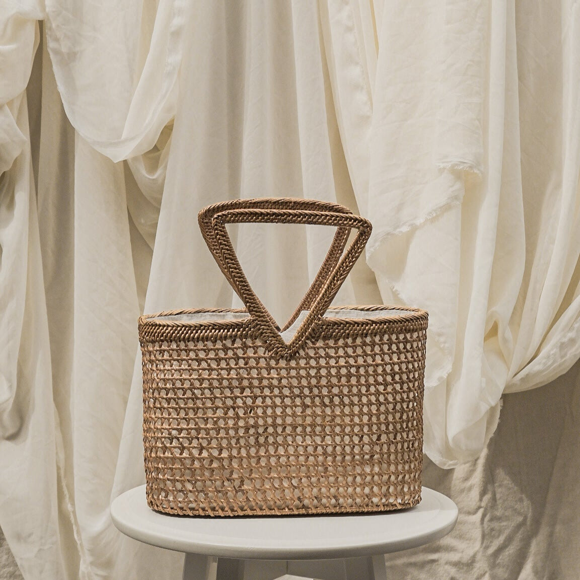 Woven basket with a handle on a white pedestal against a soft, neutral background