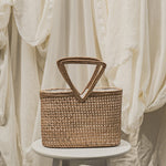 Woven basket with a handle on a white pedestal against a soft, neutral background