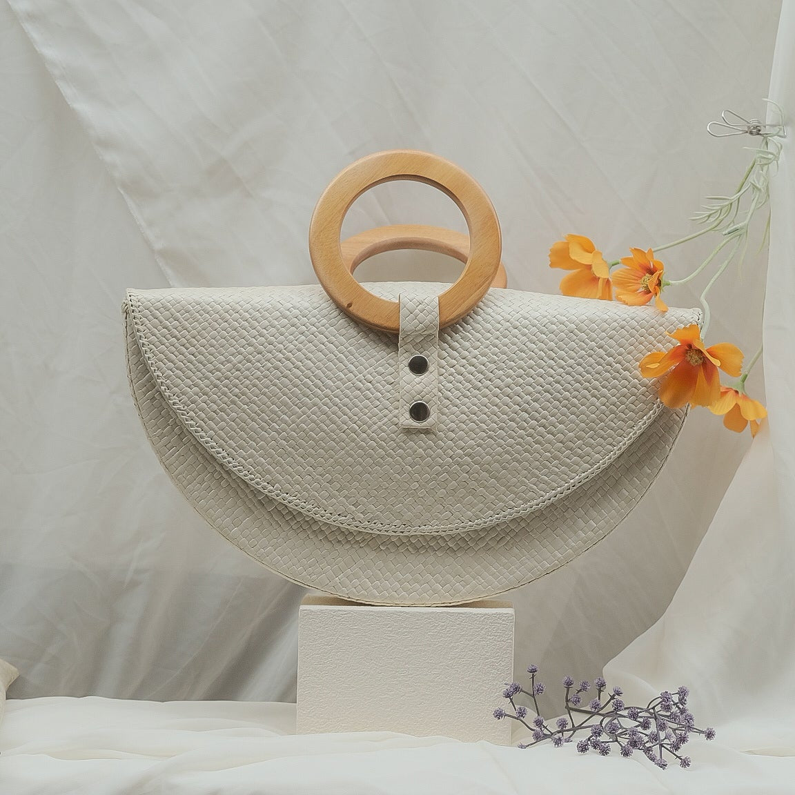 White woven handbag with wooden handle on a white background
