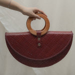 Red handbag with wooden handle held by a person against a neutral background