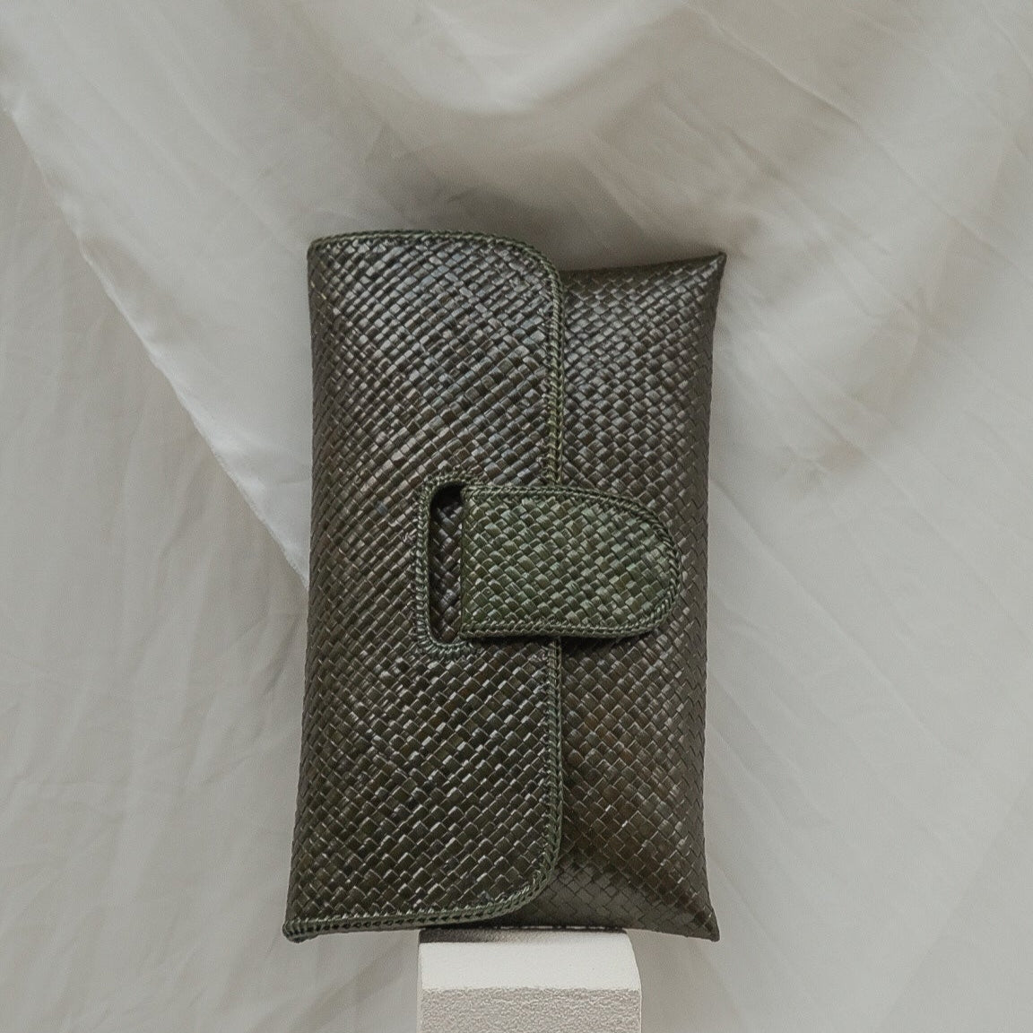Textured clutch bag on a white stand with a white fabric background