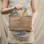 Person holding a woven handbag with a neutral background