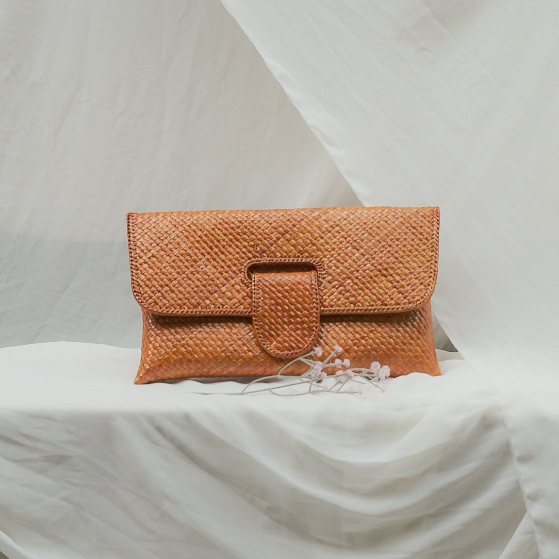 Orange woven clutch bag on a white draped surface