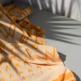Orange and beige patterned blanket on a gray surface with shadows