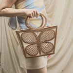 Person holding a woven handbag with a neutral background