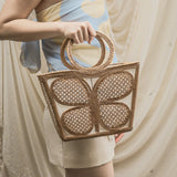 Person holding a woven handbag with a neutral background