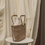Woven basket with a sheer fabric drawstring on a white stool against a draped curtain background
