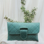 Teal clutch bag with floral arrangement on a white draped background