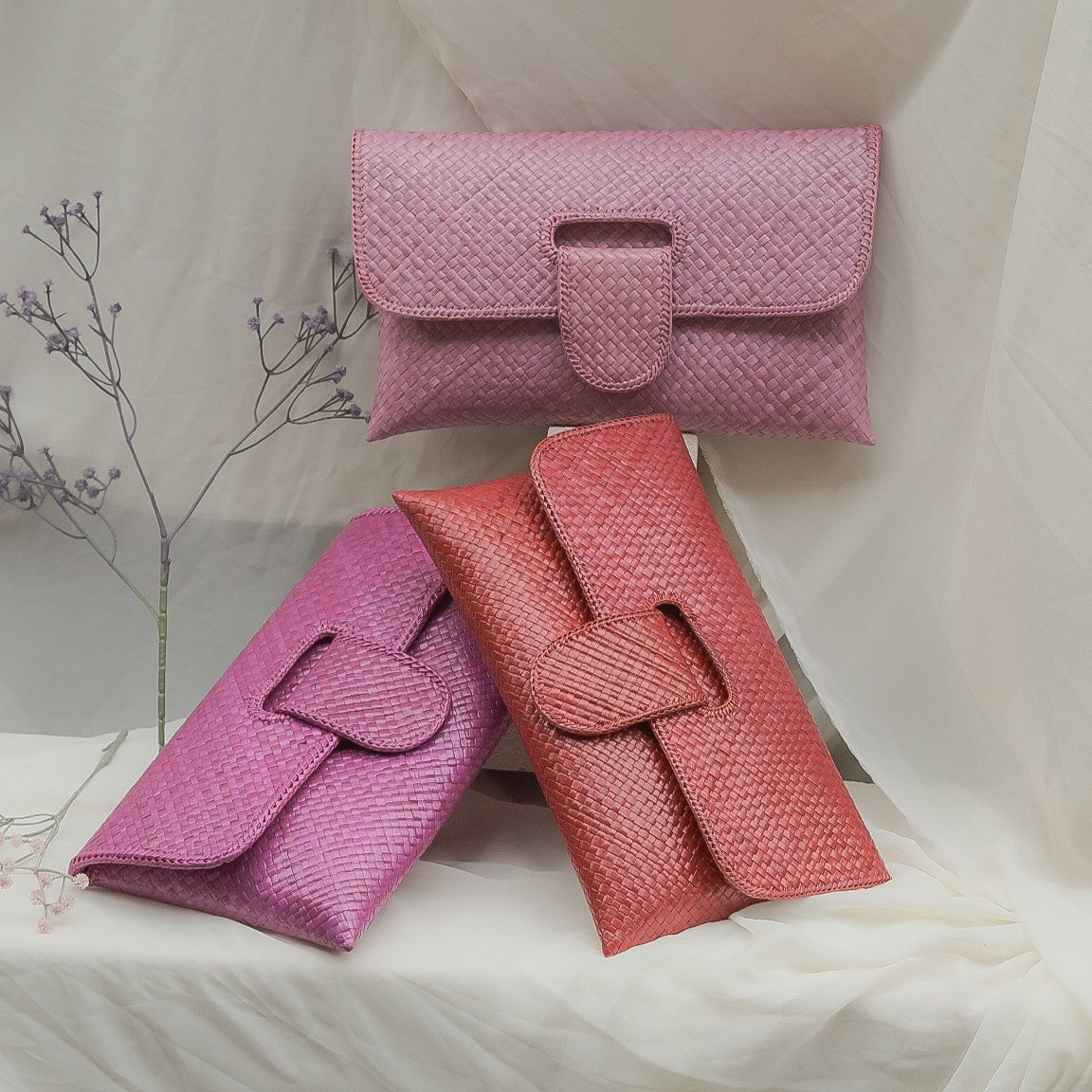 Three pink textured handbags on a white fabric background