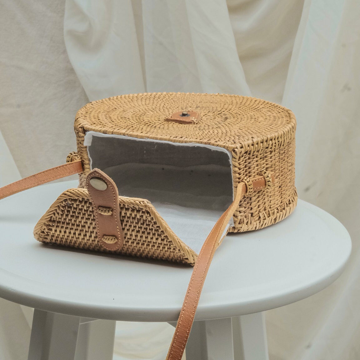 Woven handbag with a strap on a white stool against a neutral background