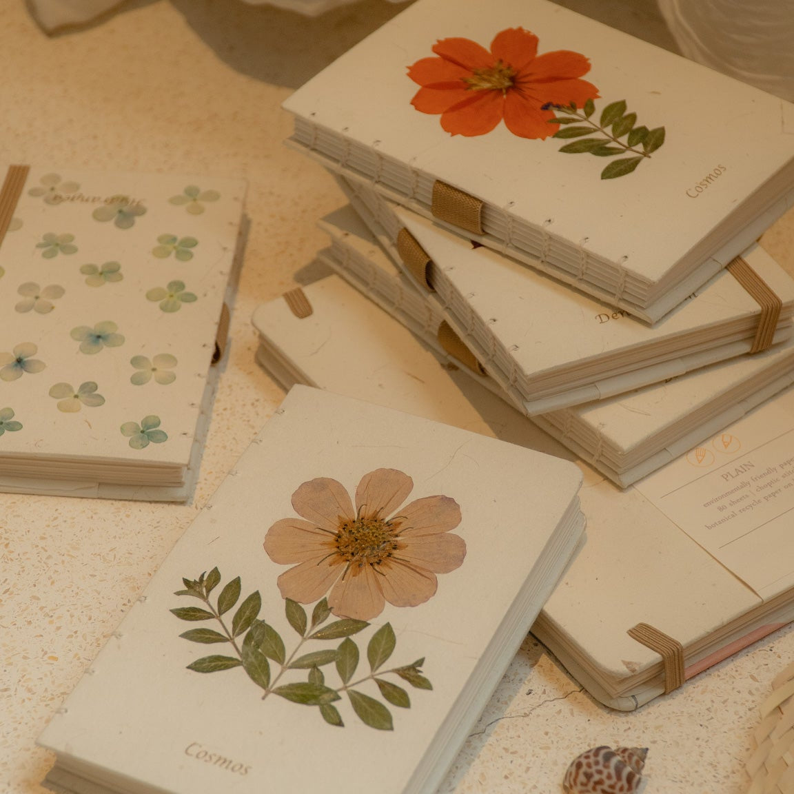 Notebooks with floral designs on a textured surface with a pen.