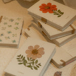 Notebooks with floral designs on a textured surface with a pen.