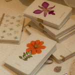 Small notebooks with pressed flowers on a textured surface with a pen.