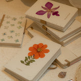 Small notebooks with pressed flowers on a textured surface with a pen.