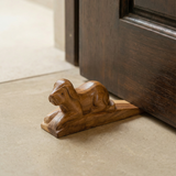 Wooden door stopper shaped like a dog on a carpeted floor next to a wooden door.