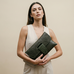 Woman holding a dark green woven clutch against a beige background