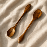 Two wooden spoons with decorative leaf-shaped handles resting on a textured beige fabric background.