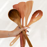Hand holding a set of wooden cooking utensils against a white background